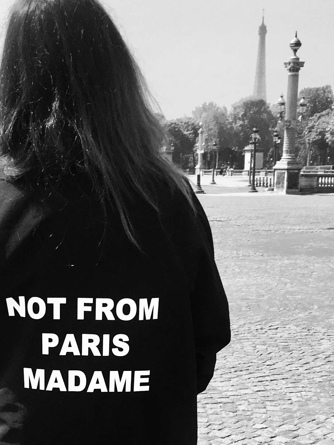 Bild von Frau Rückenansicht mit schwarzem Mantel mit weißem Aufdruck "NOT FROM PARIS MADAME" , Place Concorde, Paris mit Blick auf den Eifelturm, Stilberatung, Personal Shopping stil-verliebt